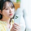 女性がスマートフォンを持って、考え込んでいる写真