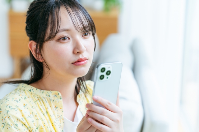 女性がスマートフォンを持って、考え込んでいる写真